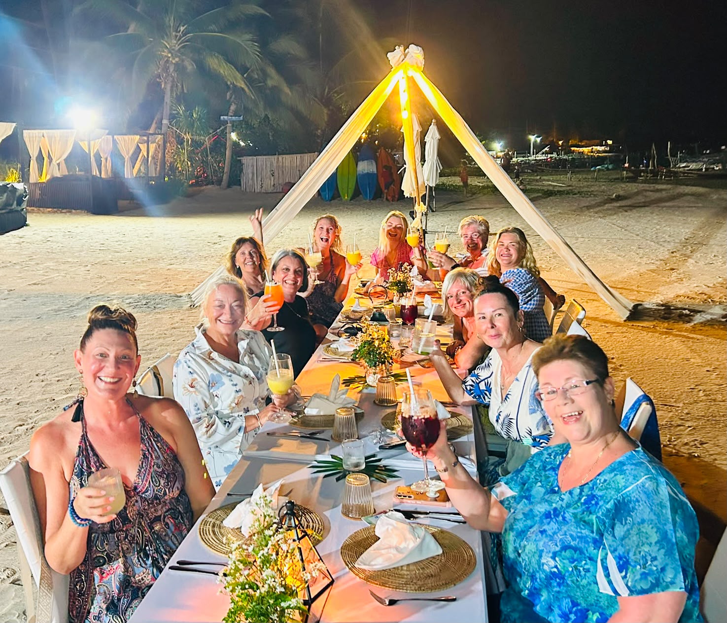 The retreat ladies toasting at a long candlelit dinner table on the beach at night